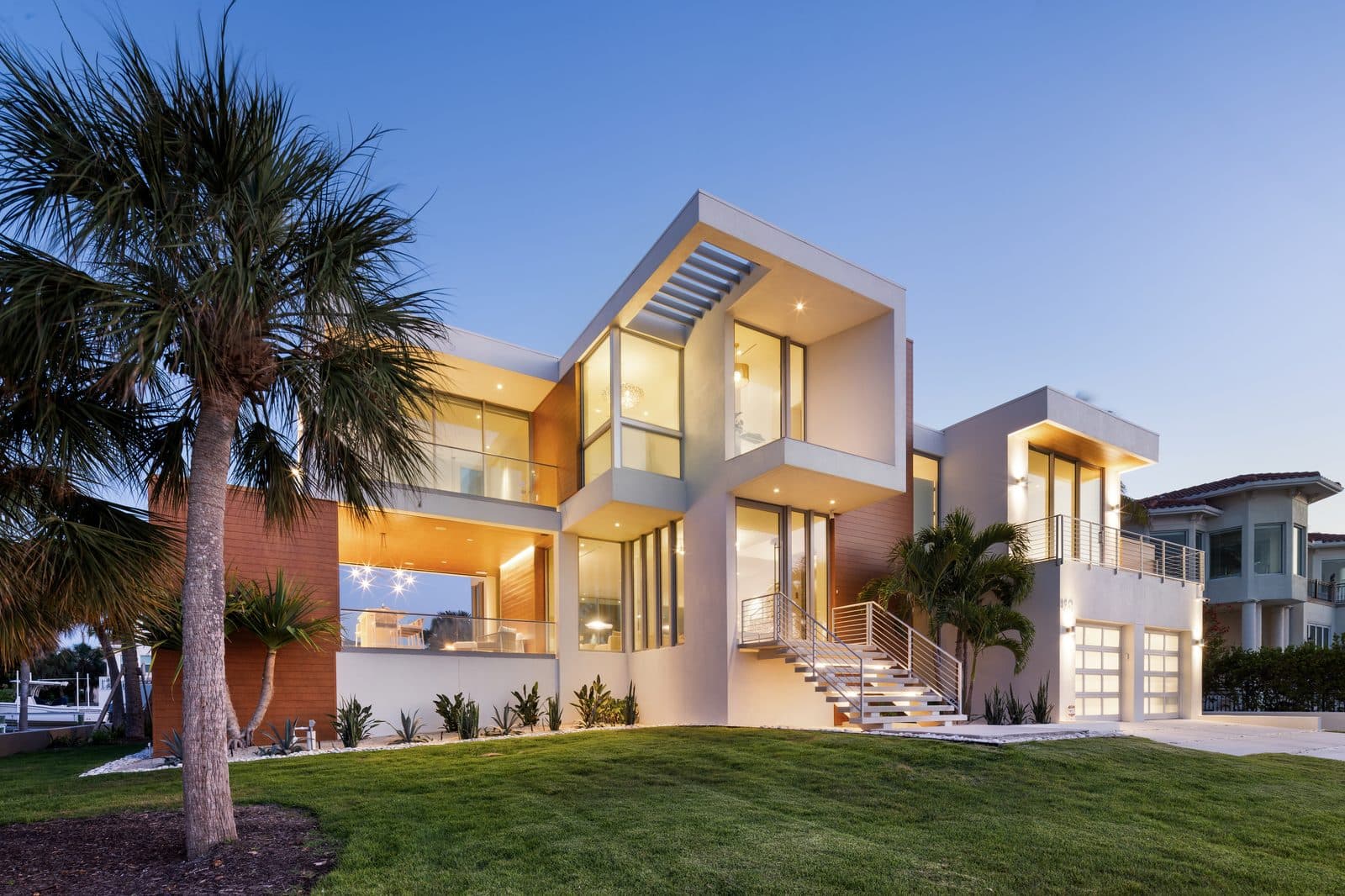 Jessmyth Cove: modern elevation at dusk, lit from within, with a palm on the lawn